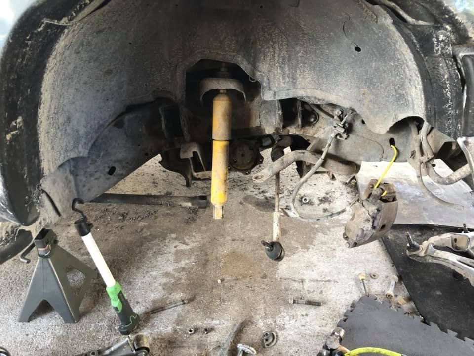 Car wheel well with removed suspension components, including a yellow shock absorber, on jack stands.