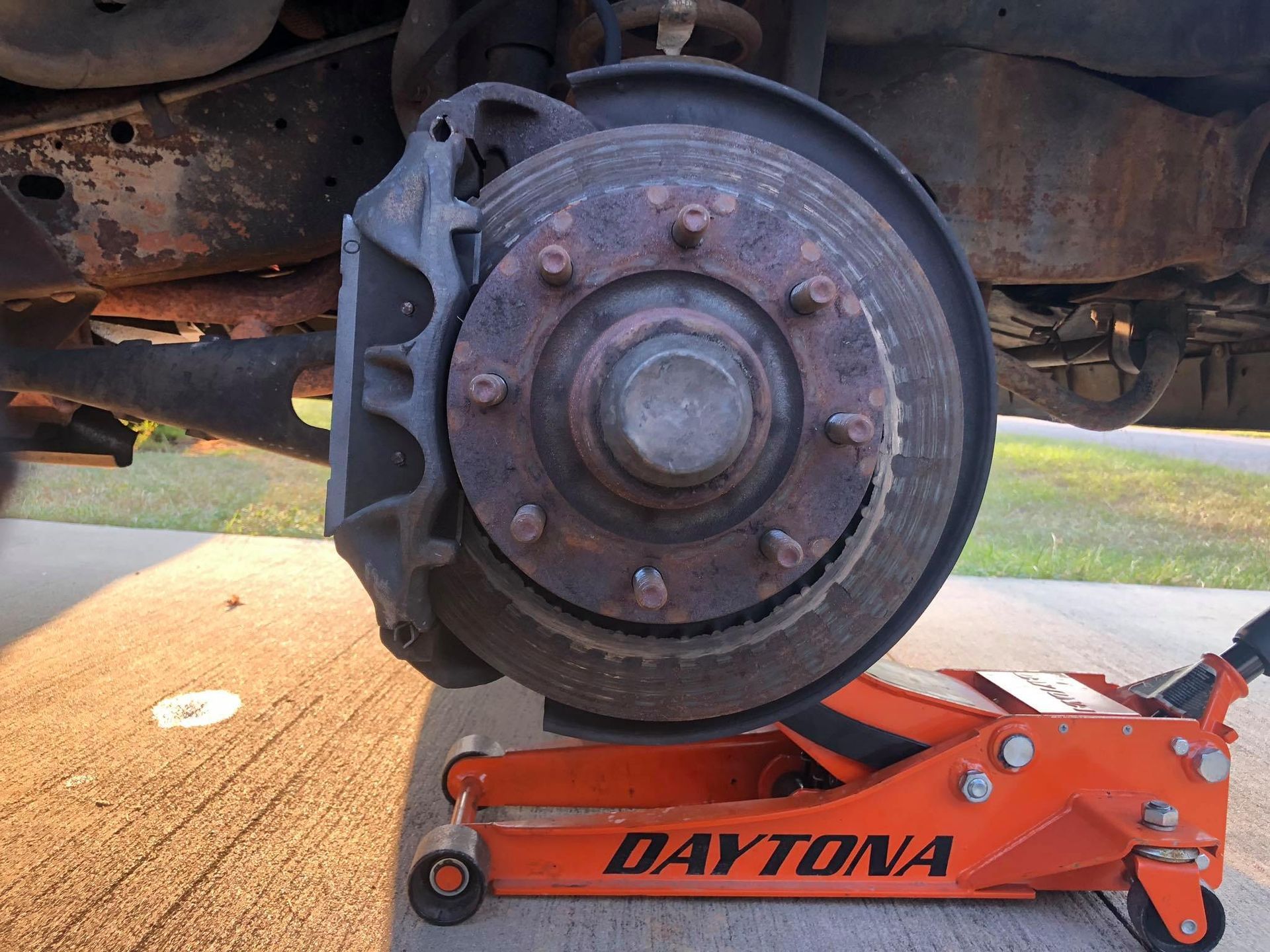 Rusty car brake rotor with caliper; orange Daytona jack supporting it.