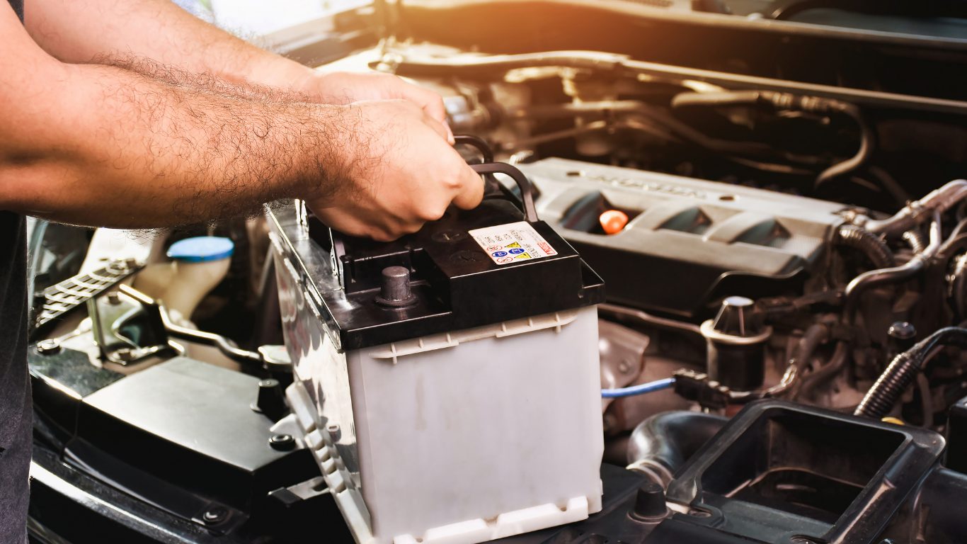 Person removing car battery from engine compartment.