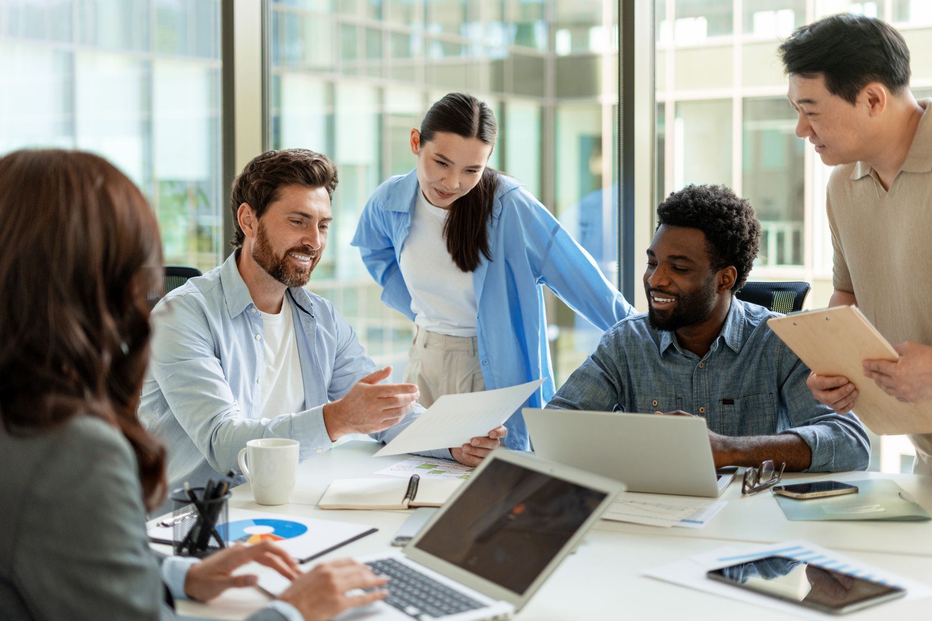 Team meeting in a bright office, with coworkers reviewing documents around a laptop.