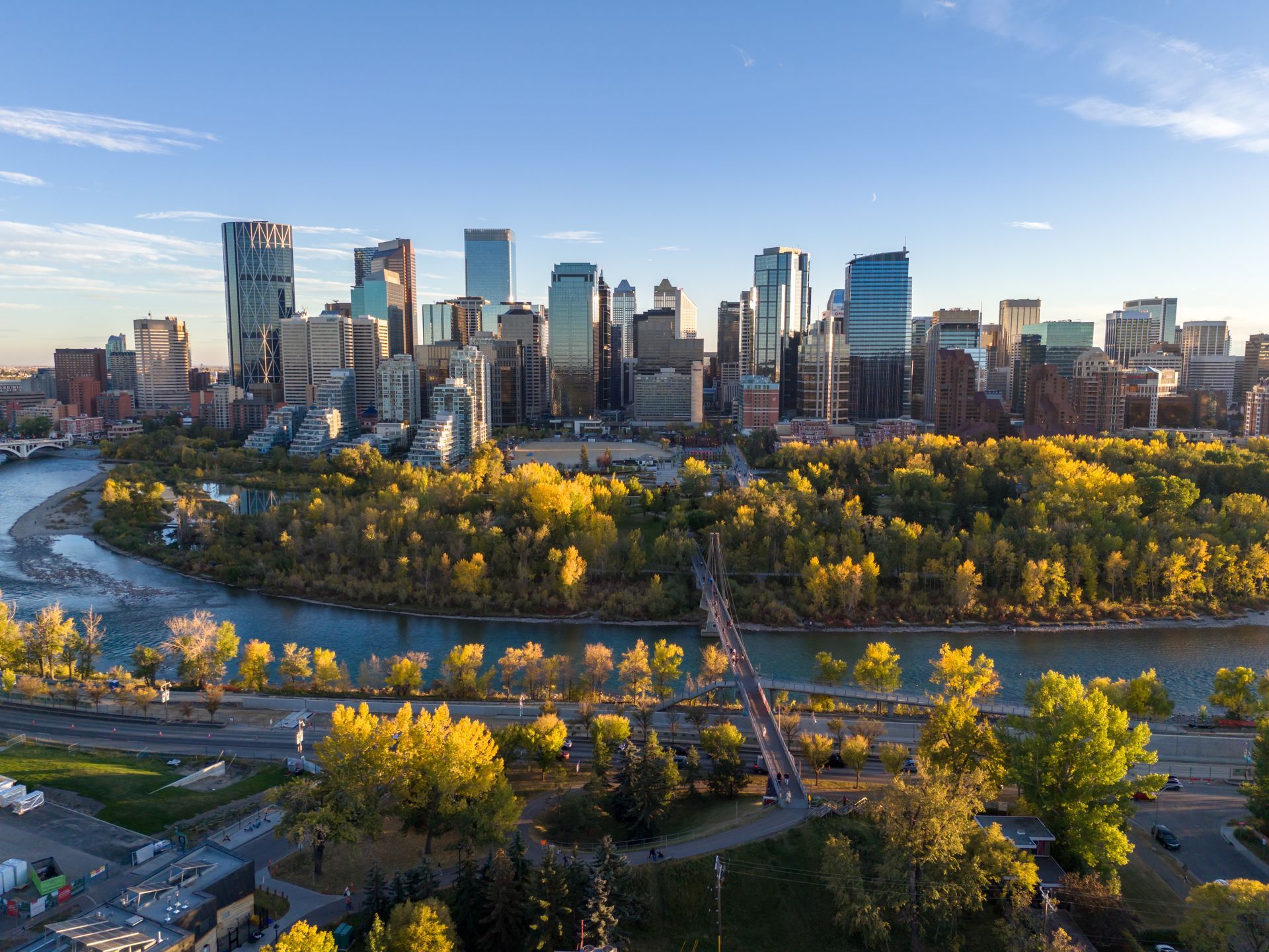 Calgary skyline with Bow River and park in foreground, under a blue sky.