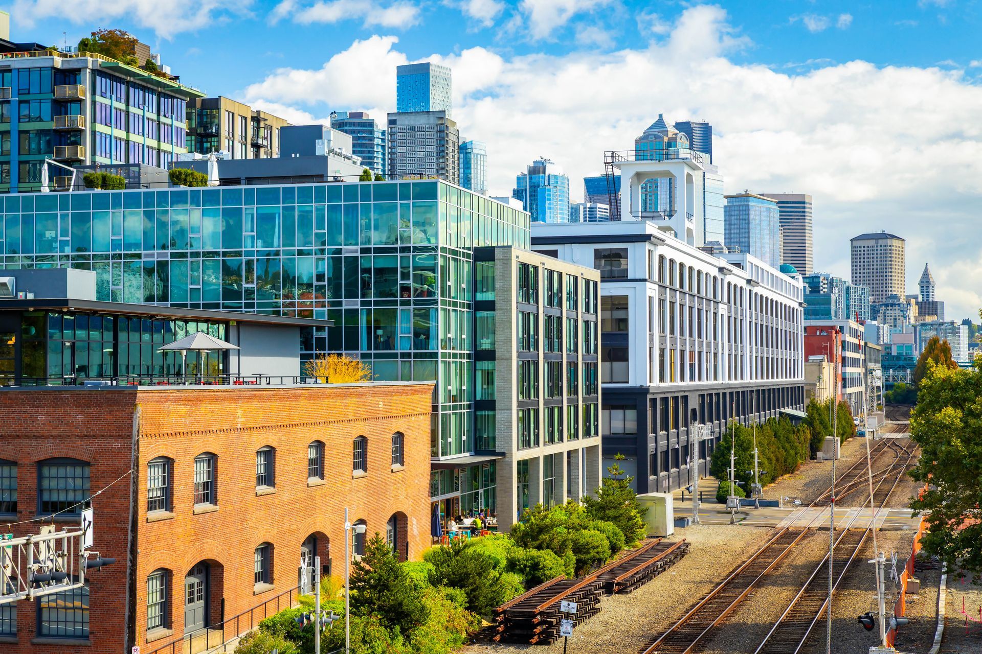 Modern glass buildings along railroad tracks in a sunny urban neighborhood
