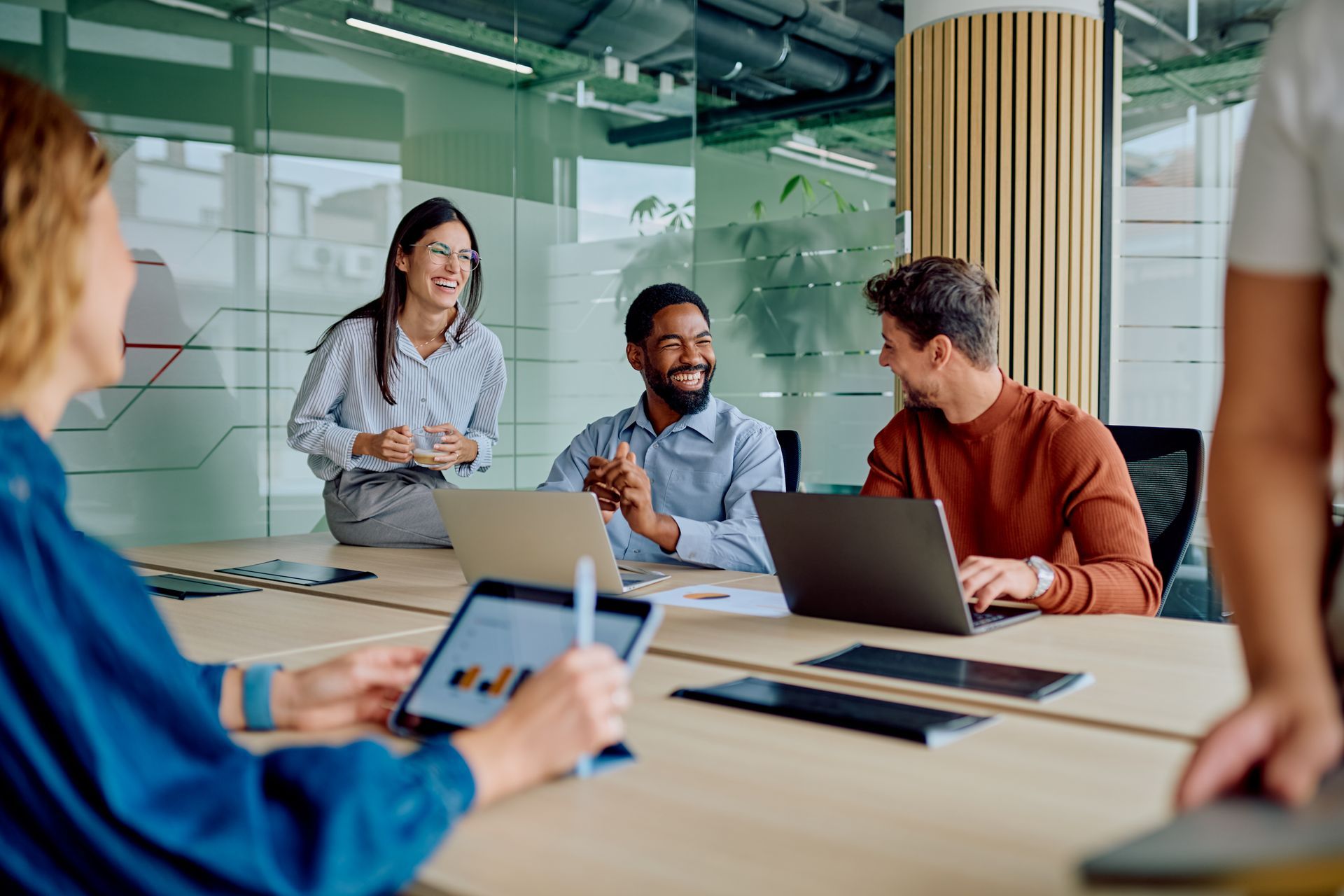 A team of four coworkers sitting at a large table in a modern office, collaborating and smiling during a discussion.