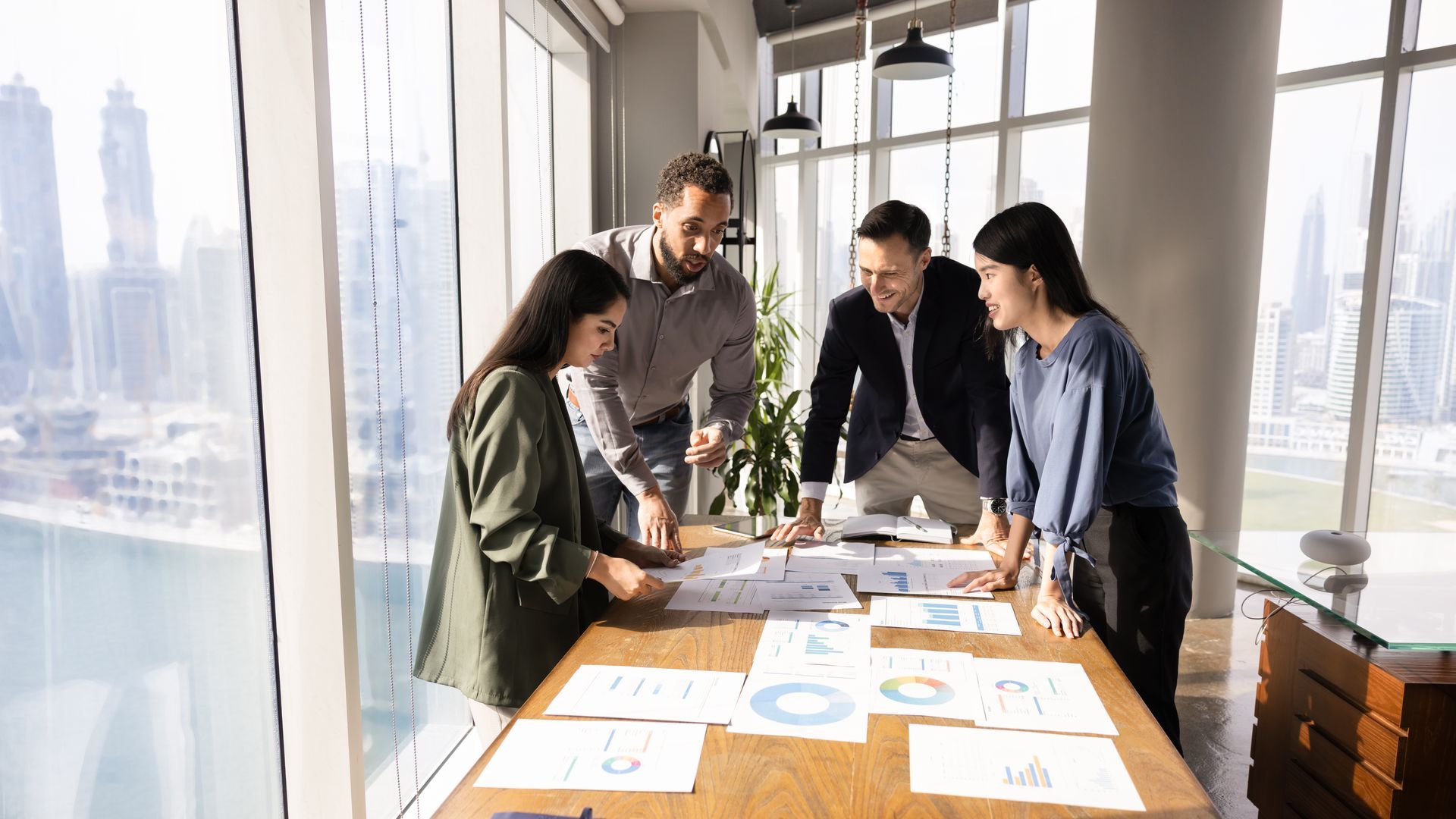 Business team reviewing papers around a table, large windows with city view.