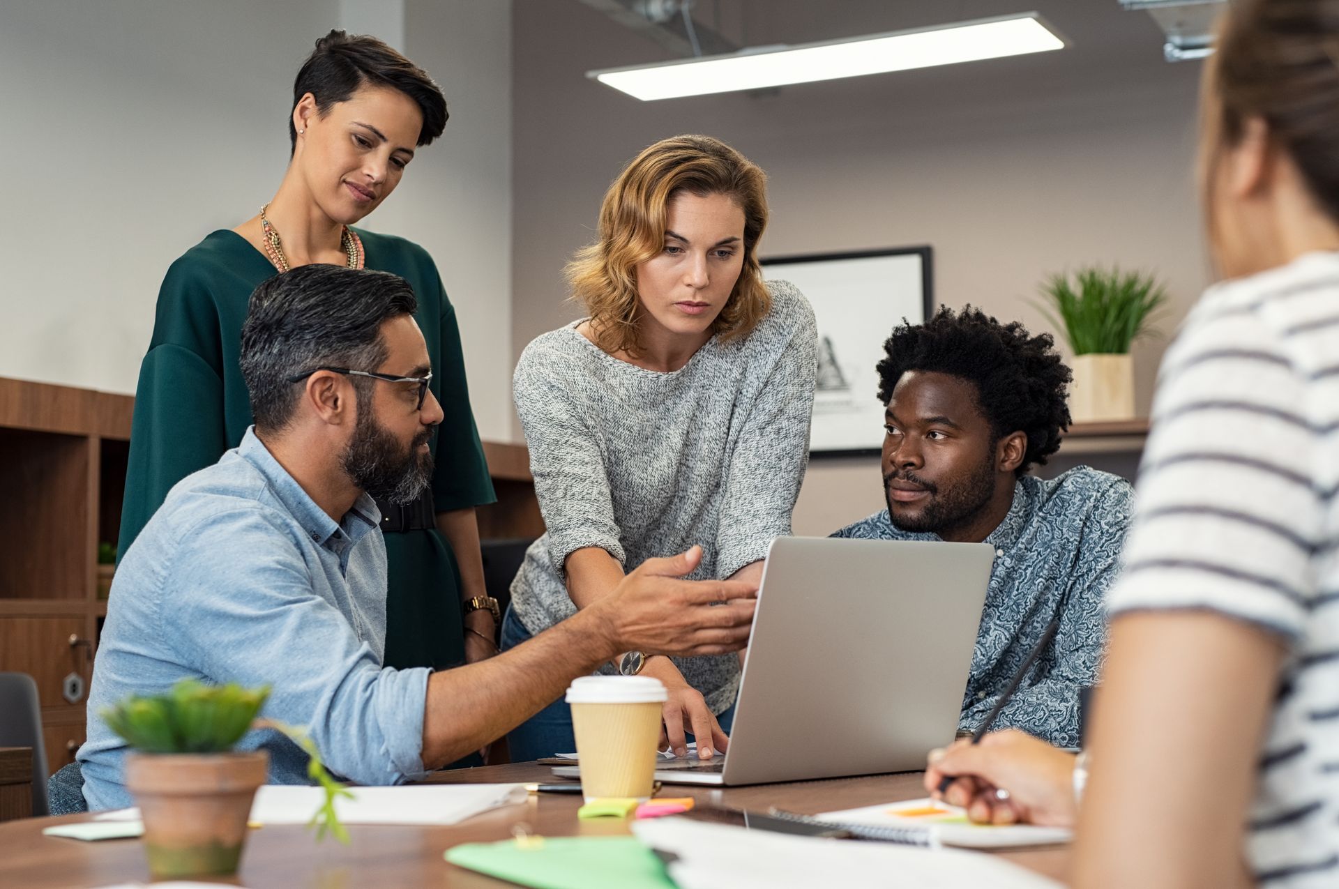 A group of people are sitting around a table looking at a laptop computer.