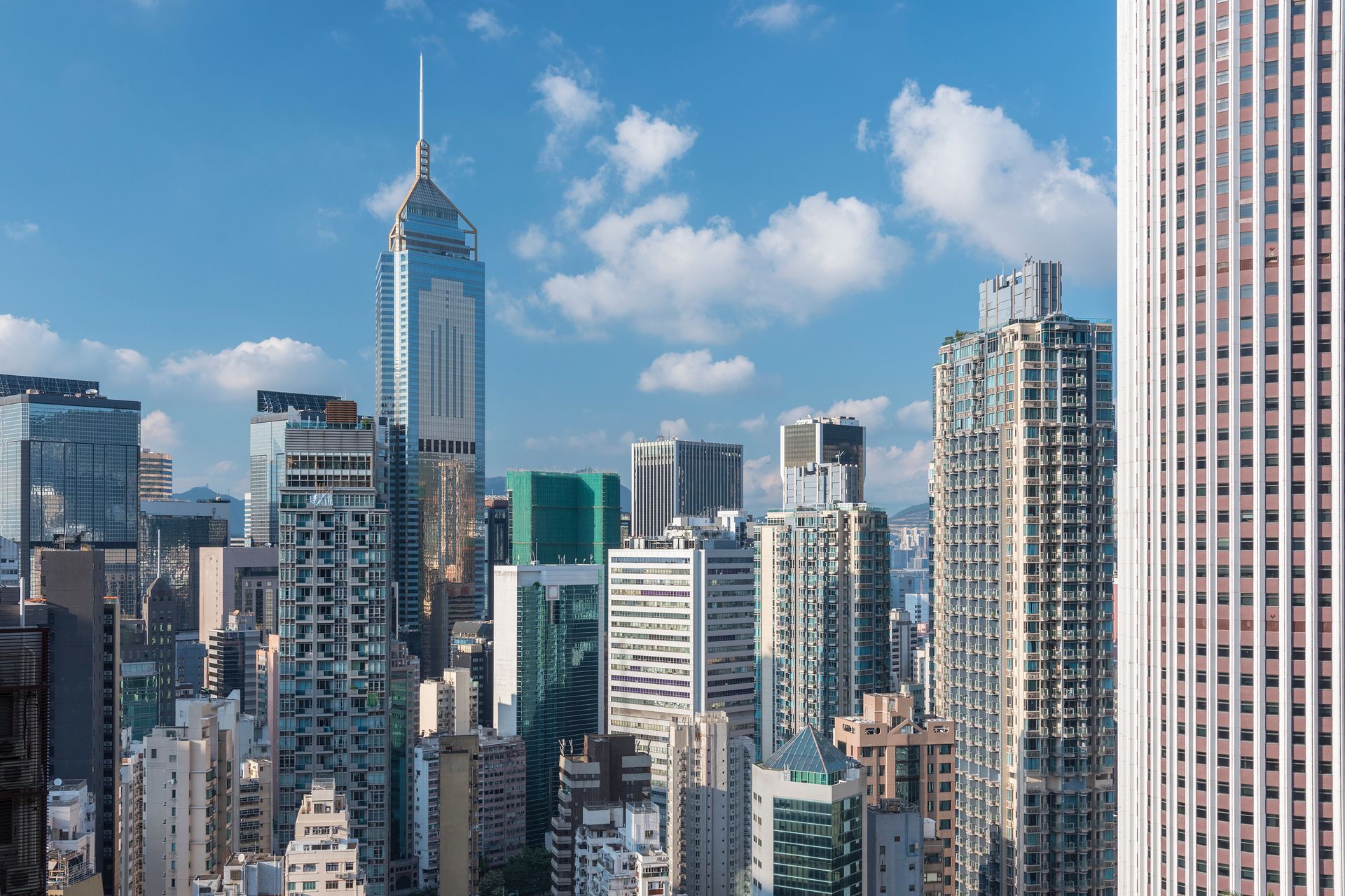 Skyline of tall modern skyscrapers under a bright blue sky with scattered clouds.