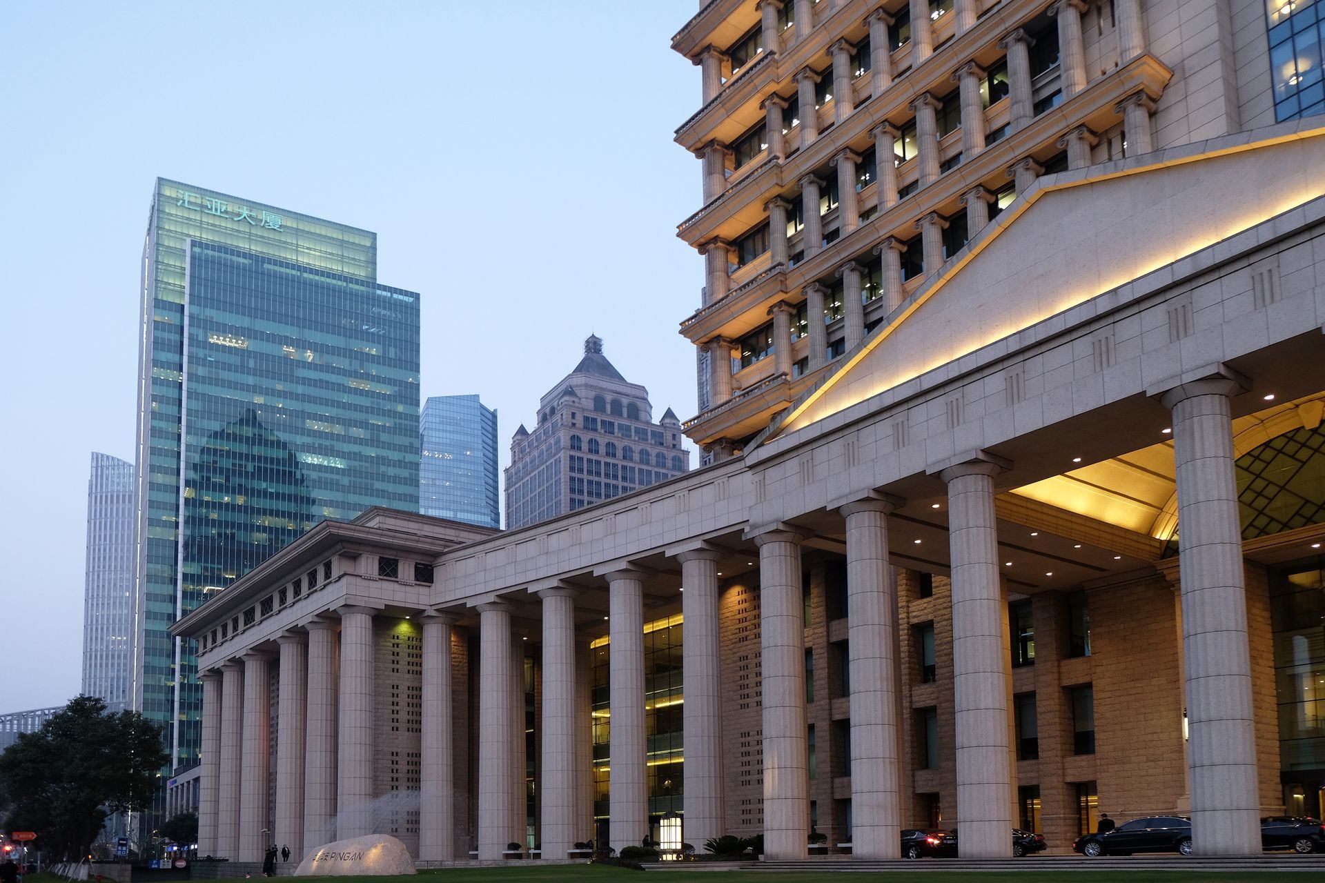 A low-angle view of a classical-style stone building with tall columns, set against a backdrop of modern glass skyscrapers.