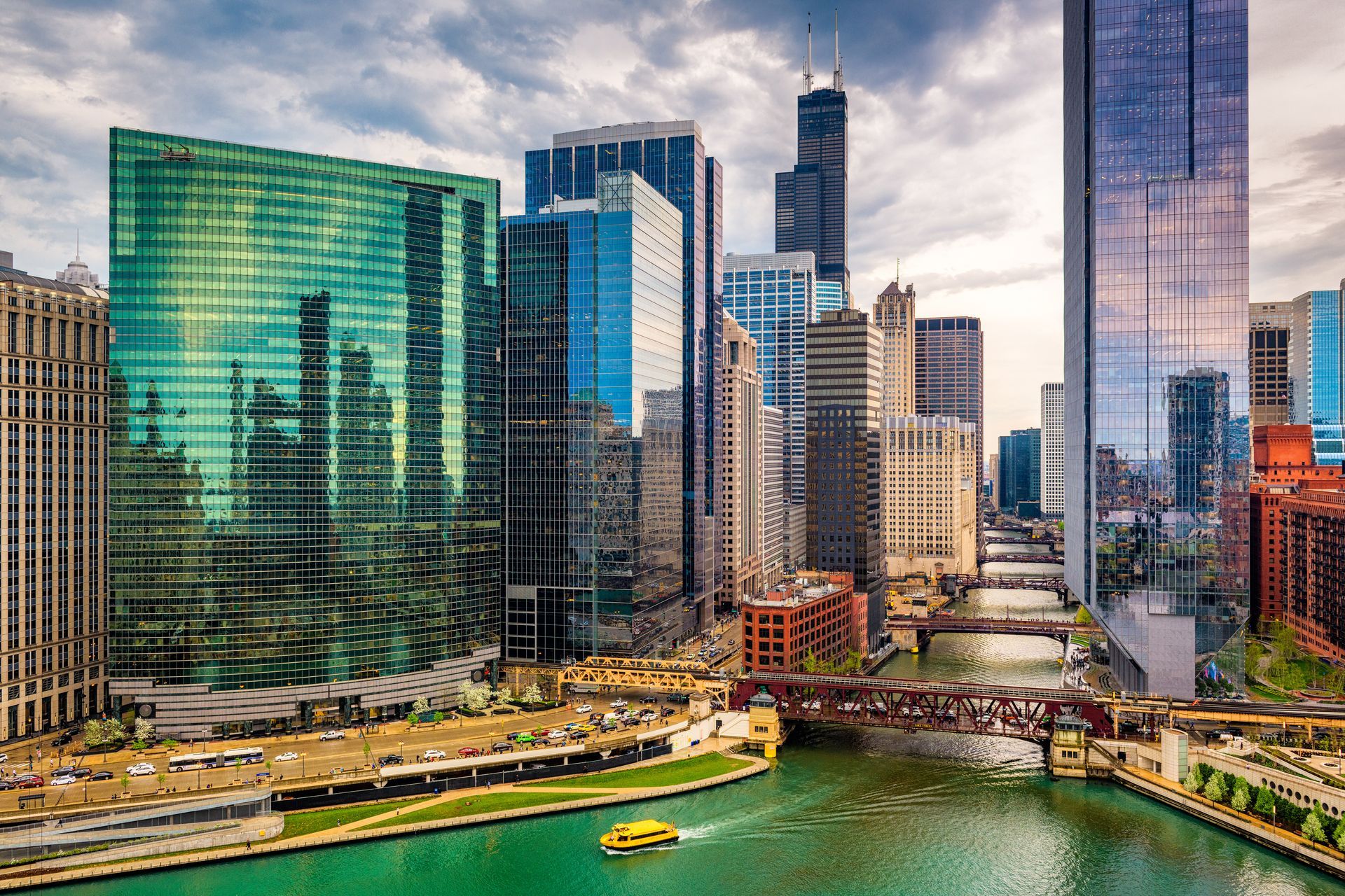 City skyline with glass skyscrapers along a green river under a cloudy sky