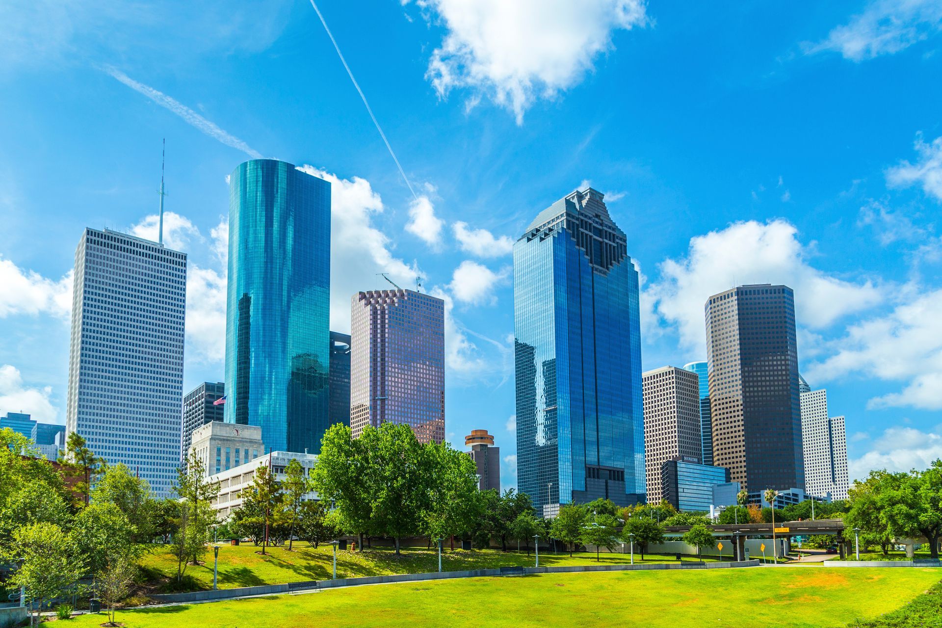 Modern city skyline with glass skyscrapers above green park under a bright blue sky