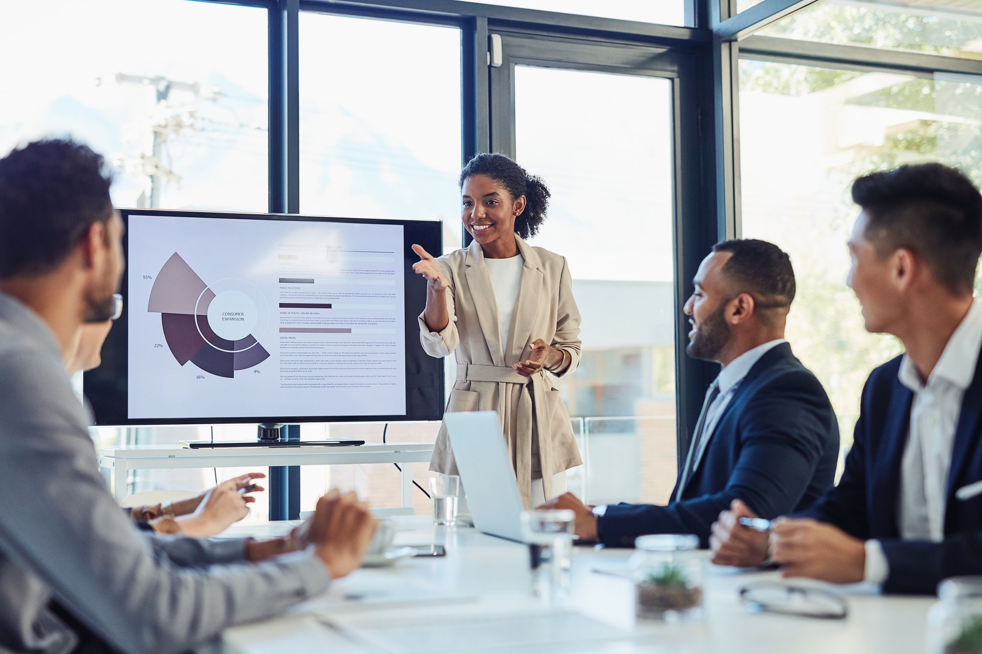 Team in a conference room listening to a presenter beside a screen with charts and graphs
