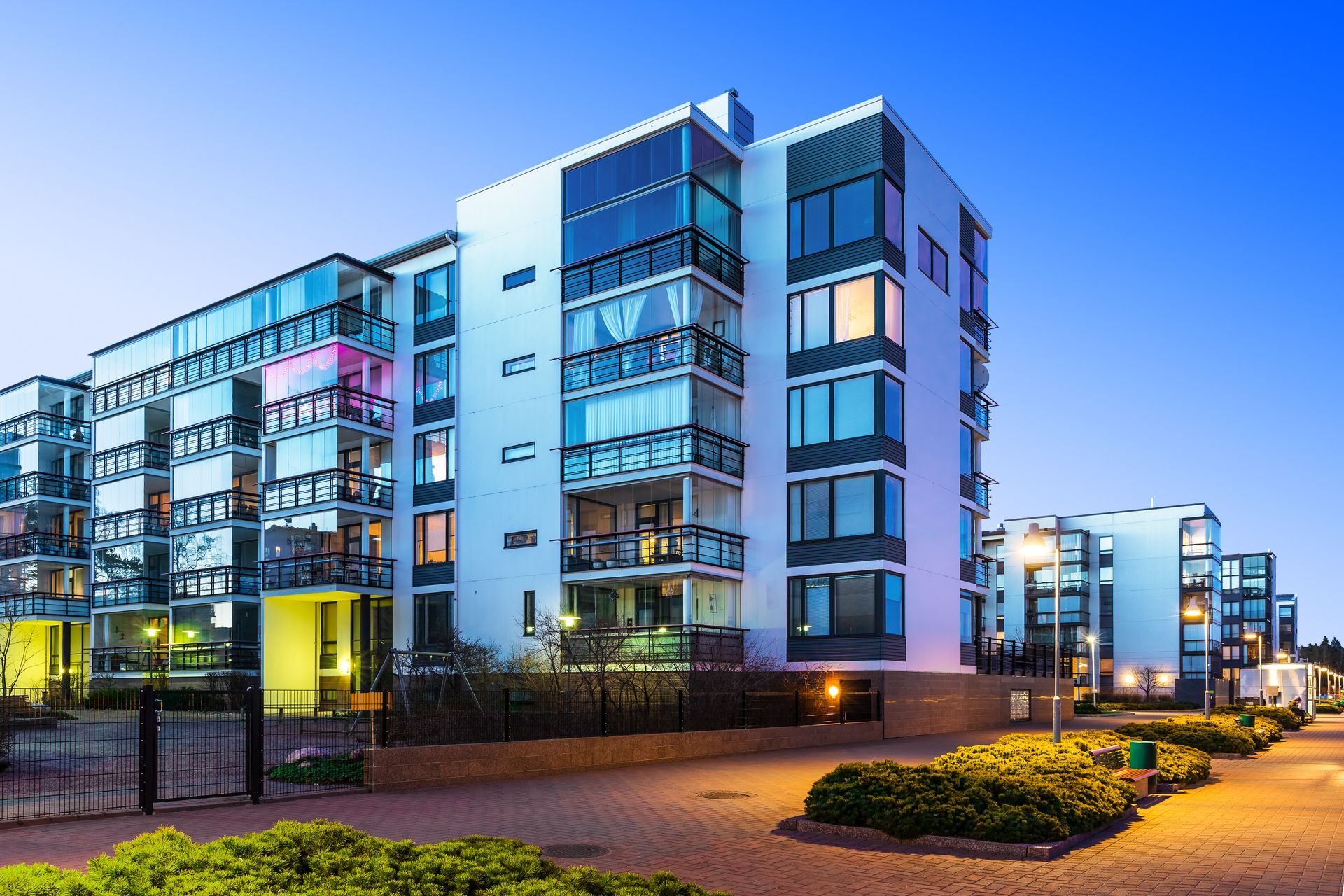 Modern white apartment buildings with glass balconies at dusk.