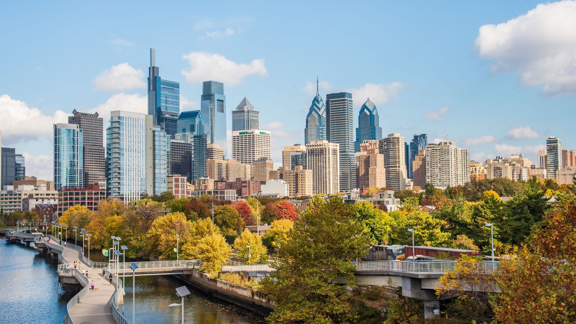 A city skyline with a river in the foreground and trees in the background.