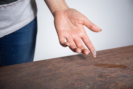 Hand reaching down to touch a wet spot on a wooden surface