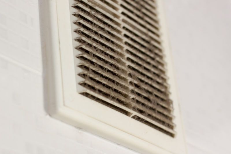 Dirty, white air vent with dust buildup on a white wall