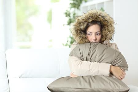 Woman bundled in winter coat and hood sits on a couch Woman bundled in winter coat and hood sits on a couch