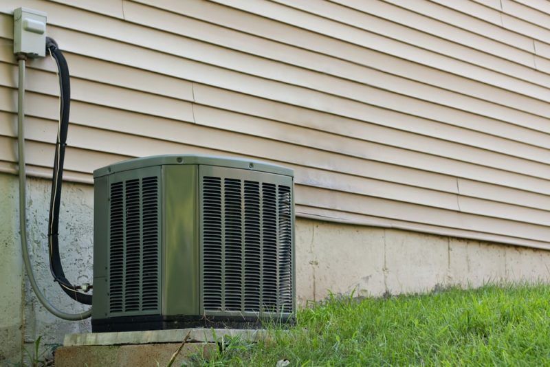 Air conditioning unit against a house with tan siding