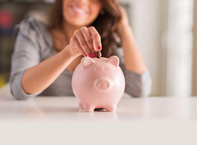 Woman smiling, inserting a coin into a pink piggy bank