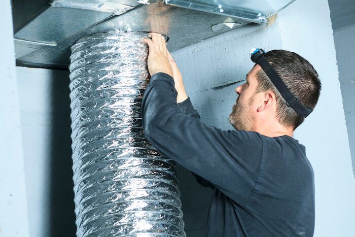 Man connecting flexible ductwork to an overhead vent