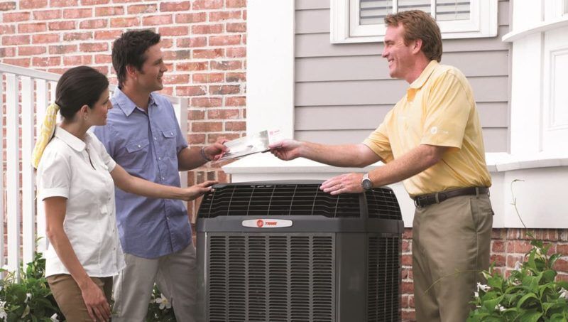 Man handing paperwork to a couple next to an outdoor HVAC unit Man handing paperwork to a couple next to an outdoor HVAC unit