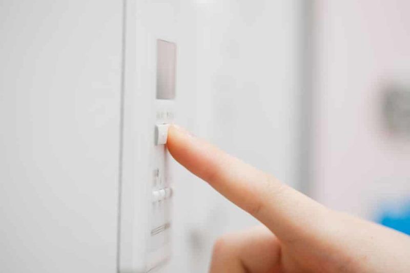 Finger presses a button on a white appliance control panel