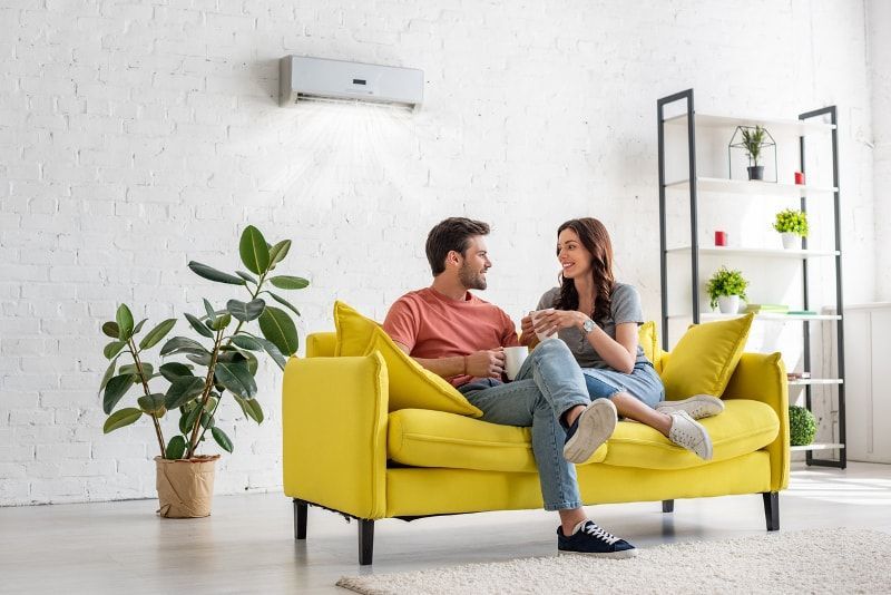 Couple sitting on yellow couch under mounted air conditioner