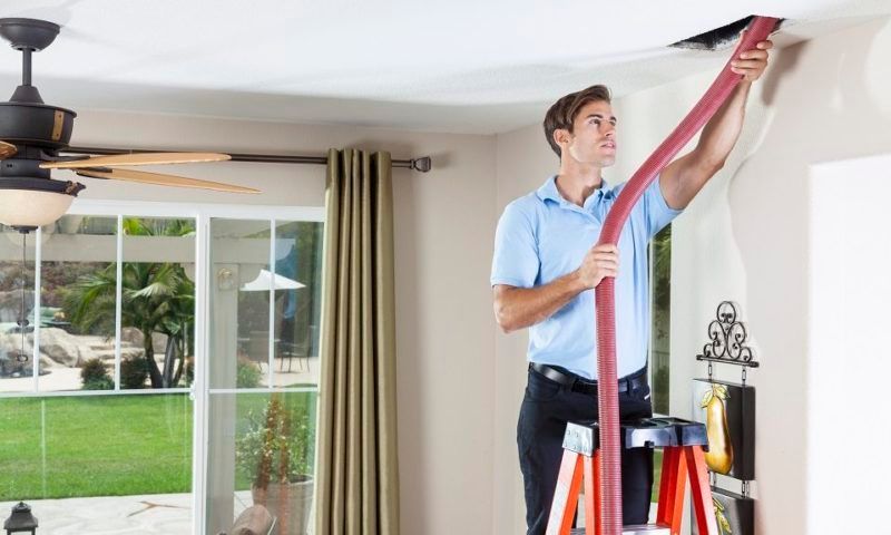 Man on ladder cleaning a ceiling vent
