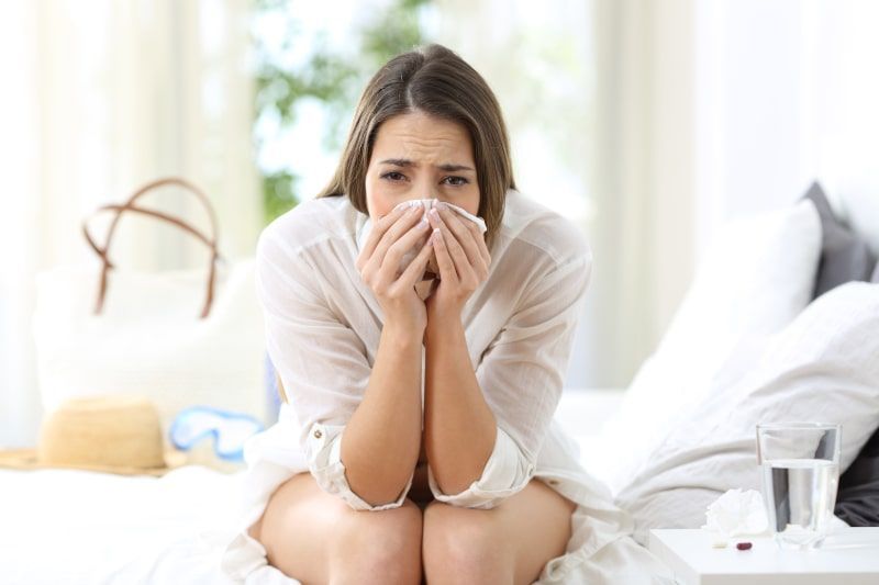 Woman on a bed, blowing nose with tissue