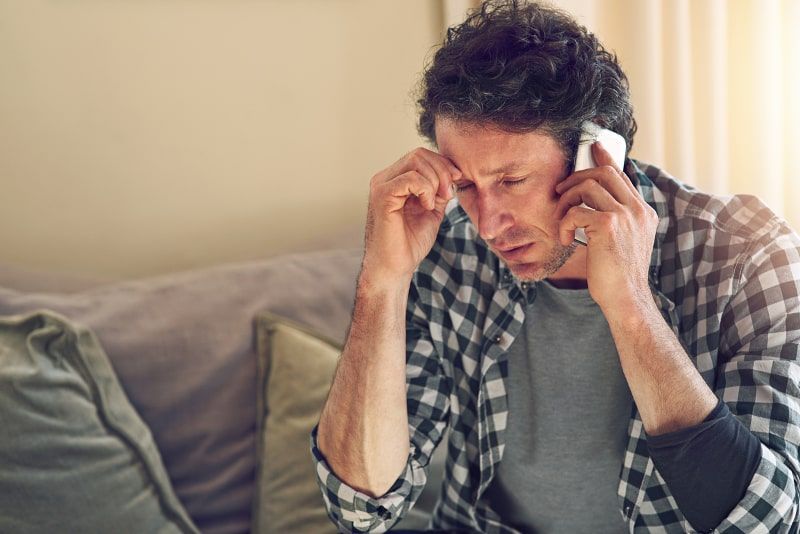 Man on phone, looking stressed, sitting on a couch