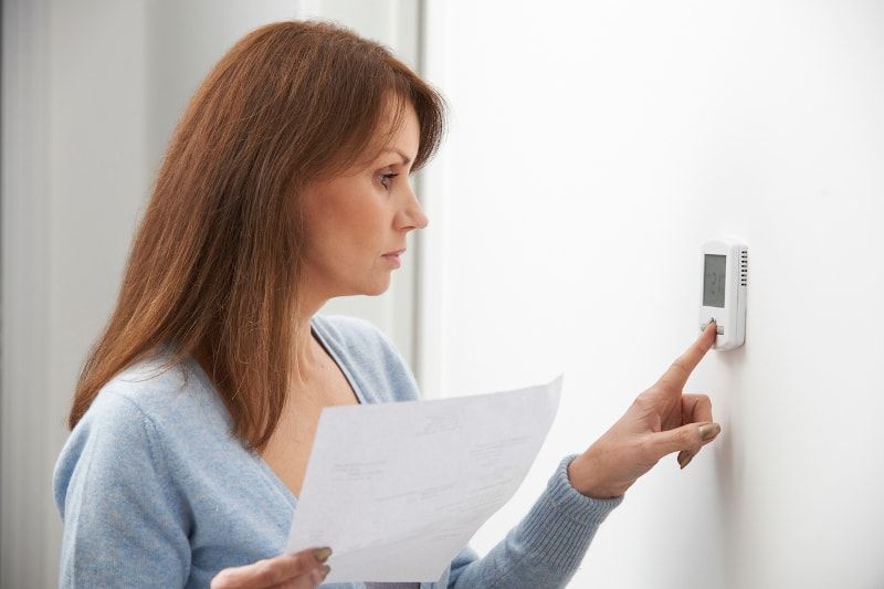 Woman holding a paper and adjusting a white thermostat on a wall