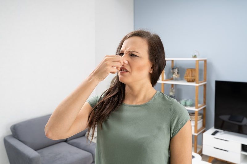 Woman holding her nose in a room, grimacing at an unpleasant smell