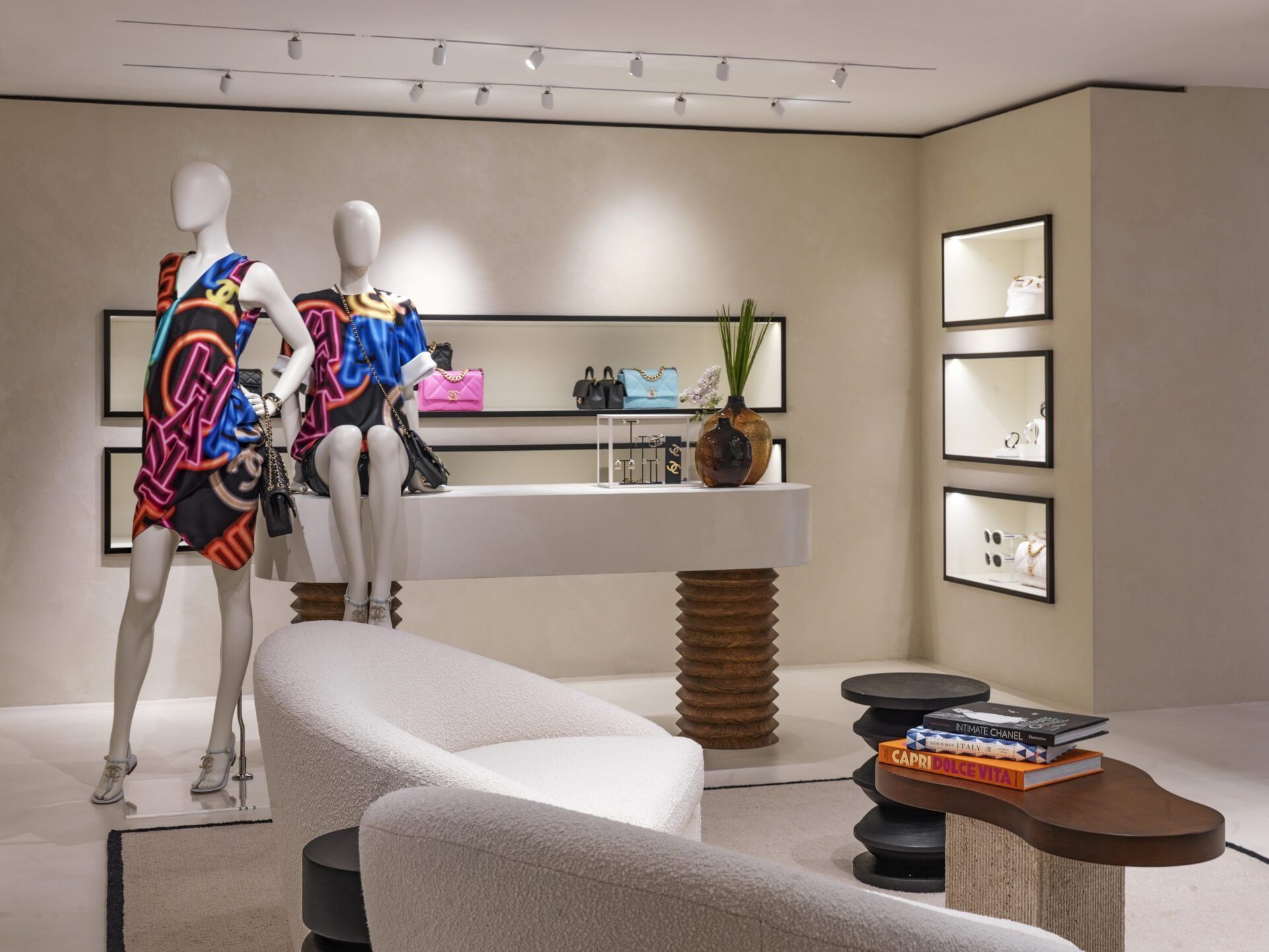 Interno di una boutique moderna con manichini che indossano abiti colorati e mobili espositivi bianchi.