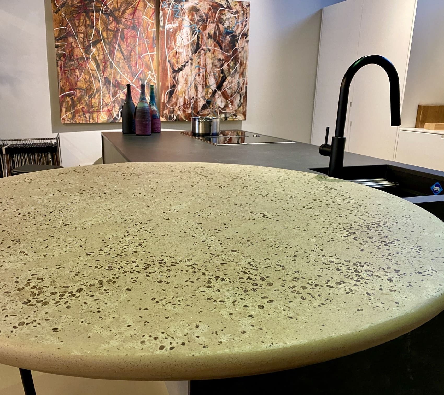 Isola cucina rotonda in pietra screziata con rubinetto nero e quadro astratto sullo sfondo.