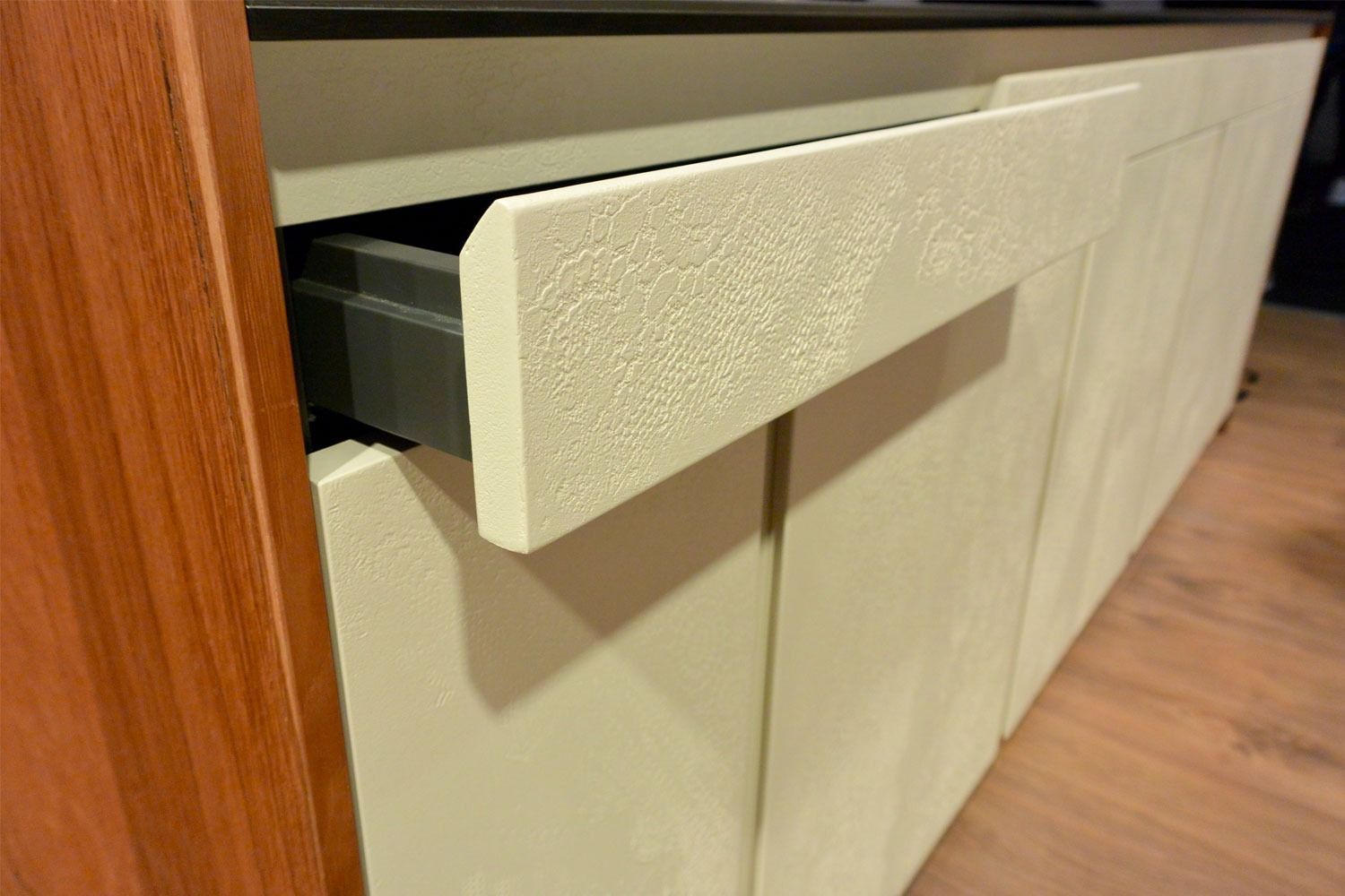 Cassetto bianco di un mobiletto sotto il piano di lavoro in cucina o in bagno, parzialmente aperto.