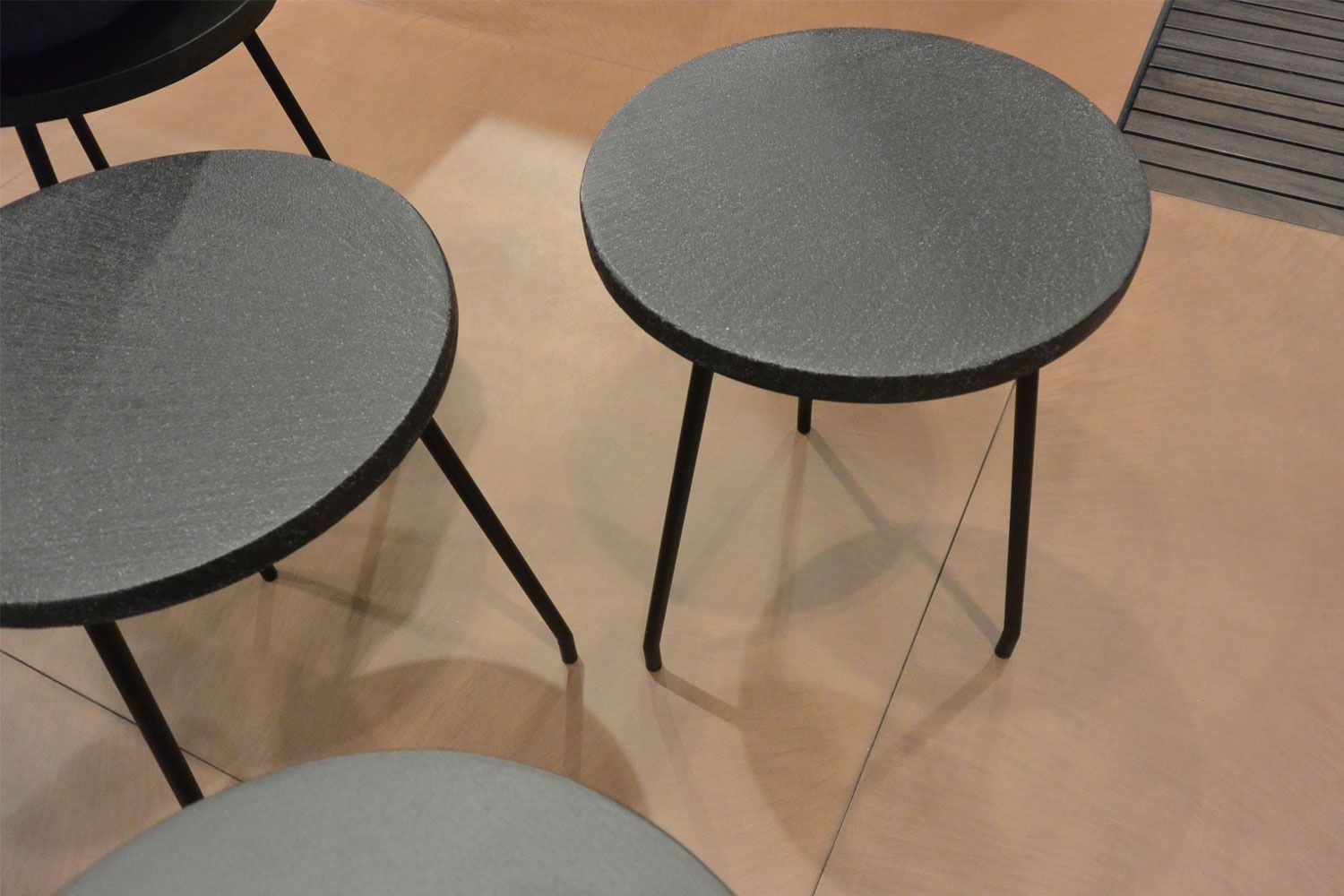 Tre sgabelli rotondi grigi con gambe nere su un pavimento piastrellato beige.