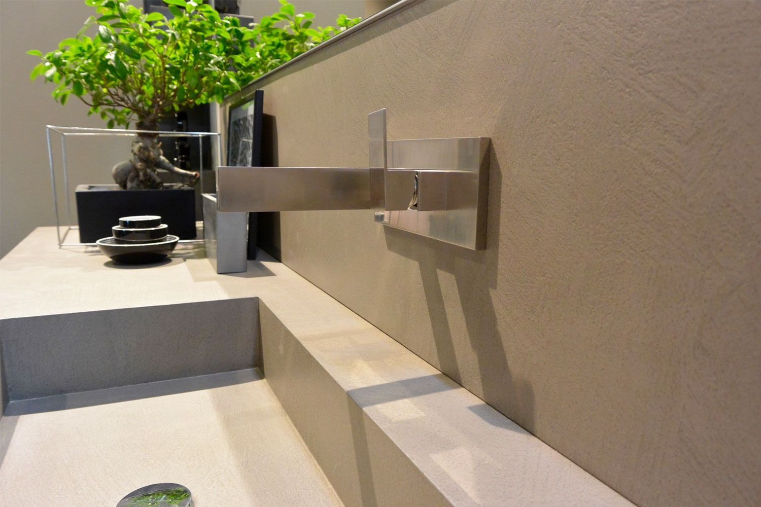 Moderno lavabo da esterno con rubinetto in acciaio inox, posizionato accanto a una pianta in vaso e un piano di lavoro in pietra.