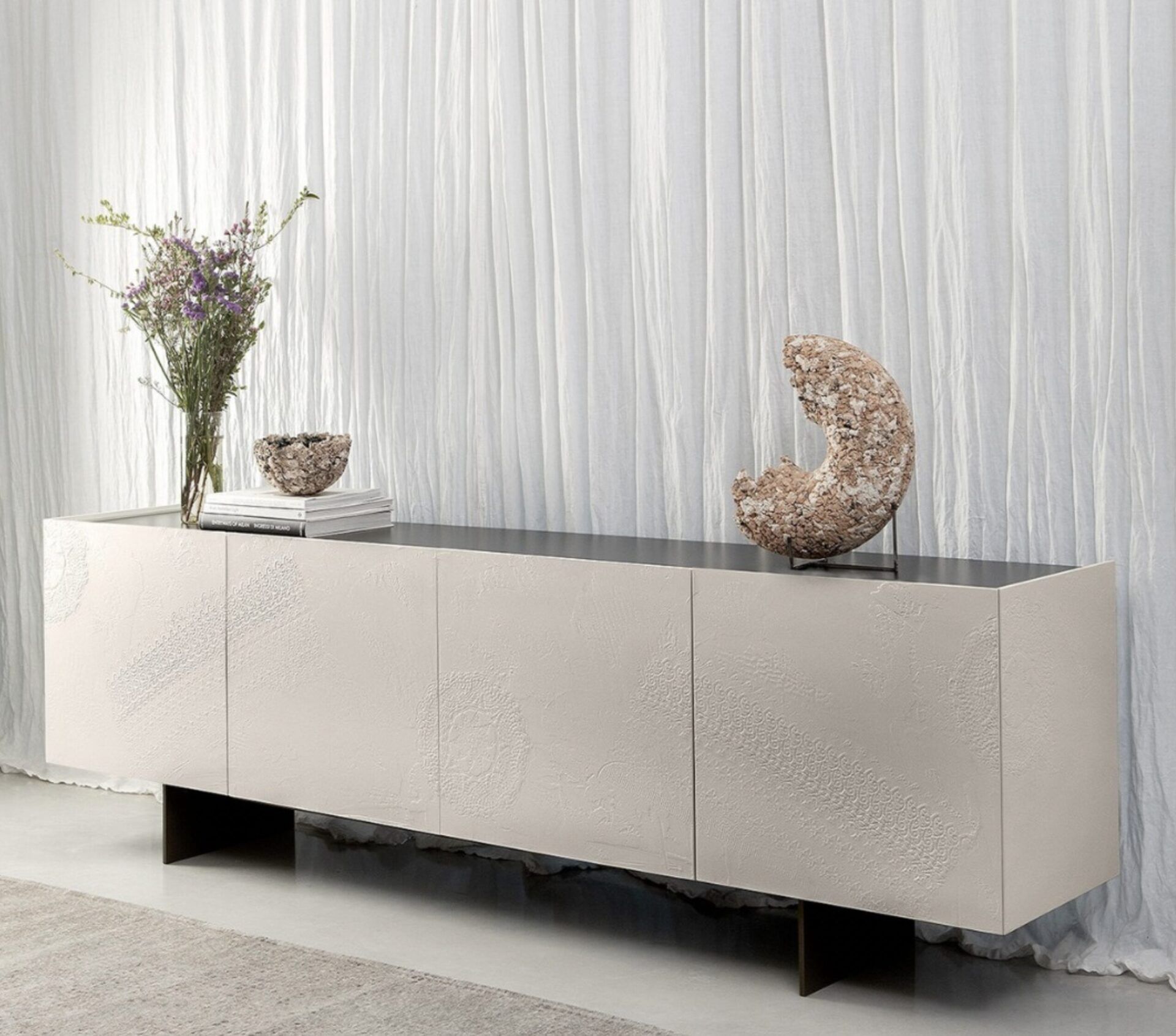Credenza moderna beige con vasi e oggetti decorativi su una parete bianca con finitura materica.
