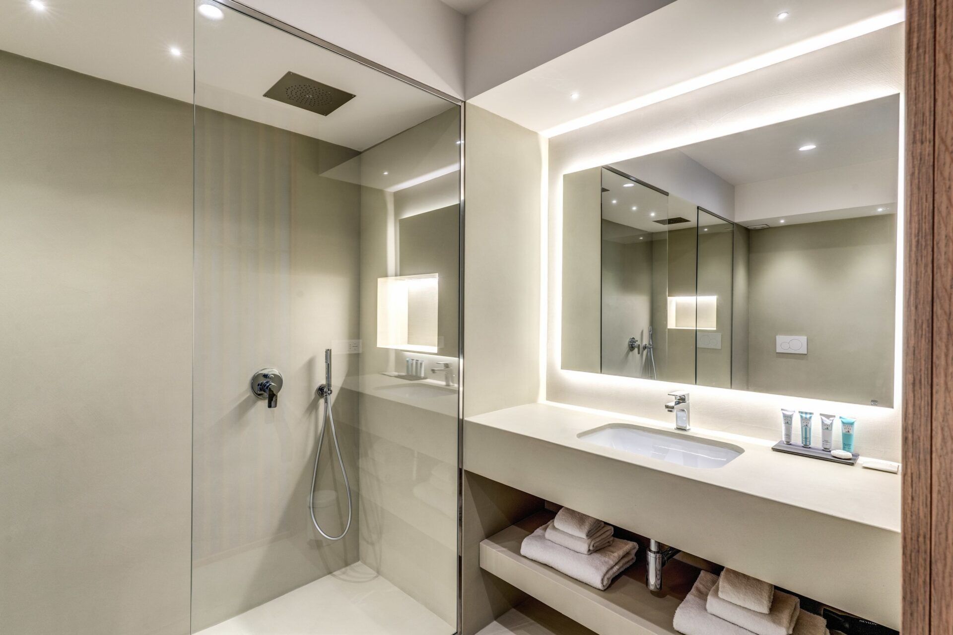 Box doccia rustico marrone con tubo flessibile bianco e mensole integrate illuminate dal basso.