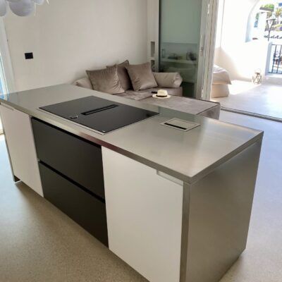 Isola cucina moderna con ripiani in acciaio inox e mobili in bianco e nero in una stanza luminosa