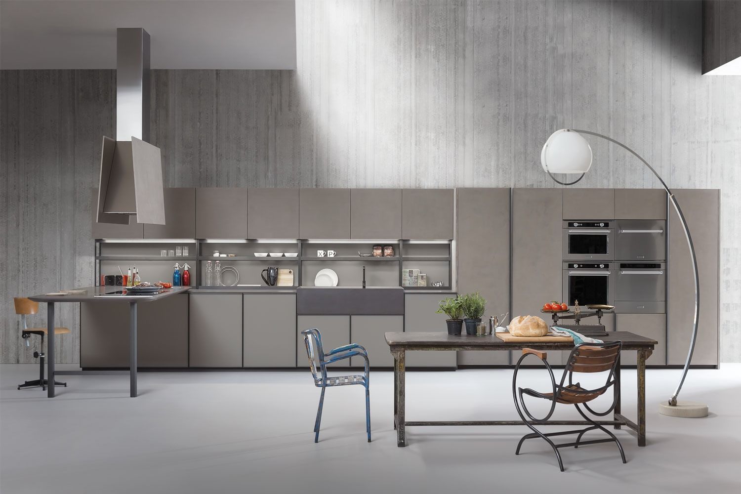 Cucina moderna grigia con isola, tavolo da pranzo, mensole e lampada da terra in un interno minimalista.