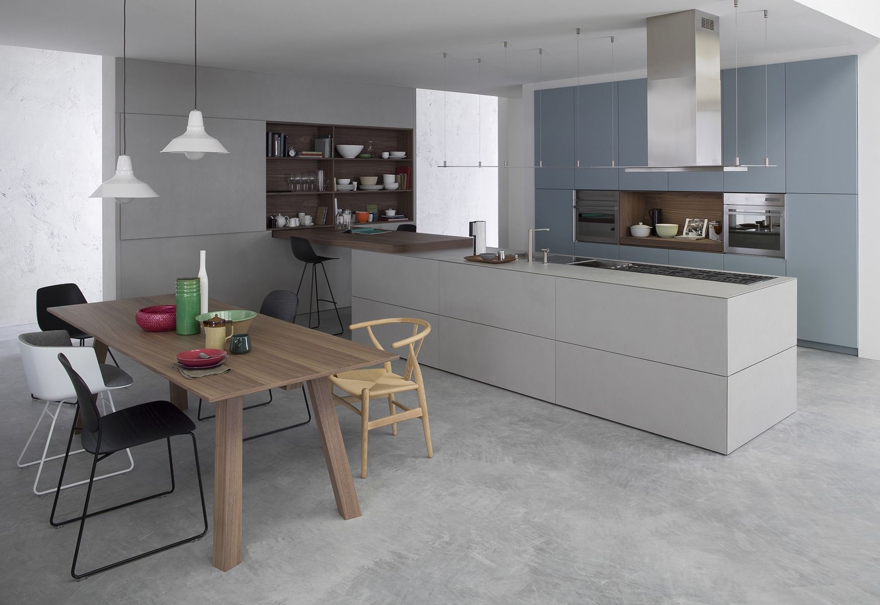 Cucina e zona pranzo moderne a pianta aperta con mobili grigi, isola bianca e tavolo in legno su pavimento in cemento.