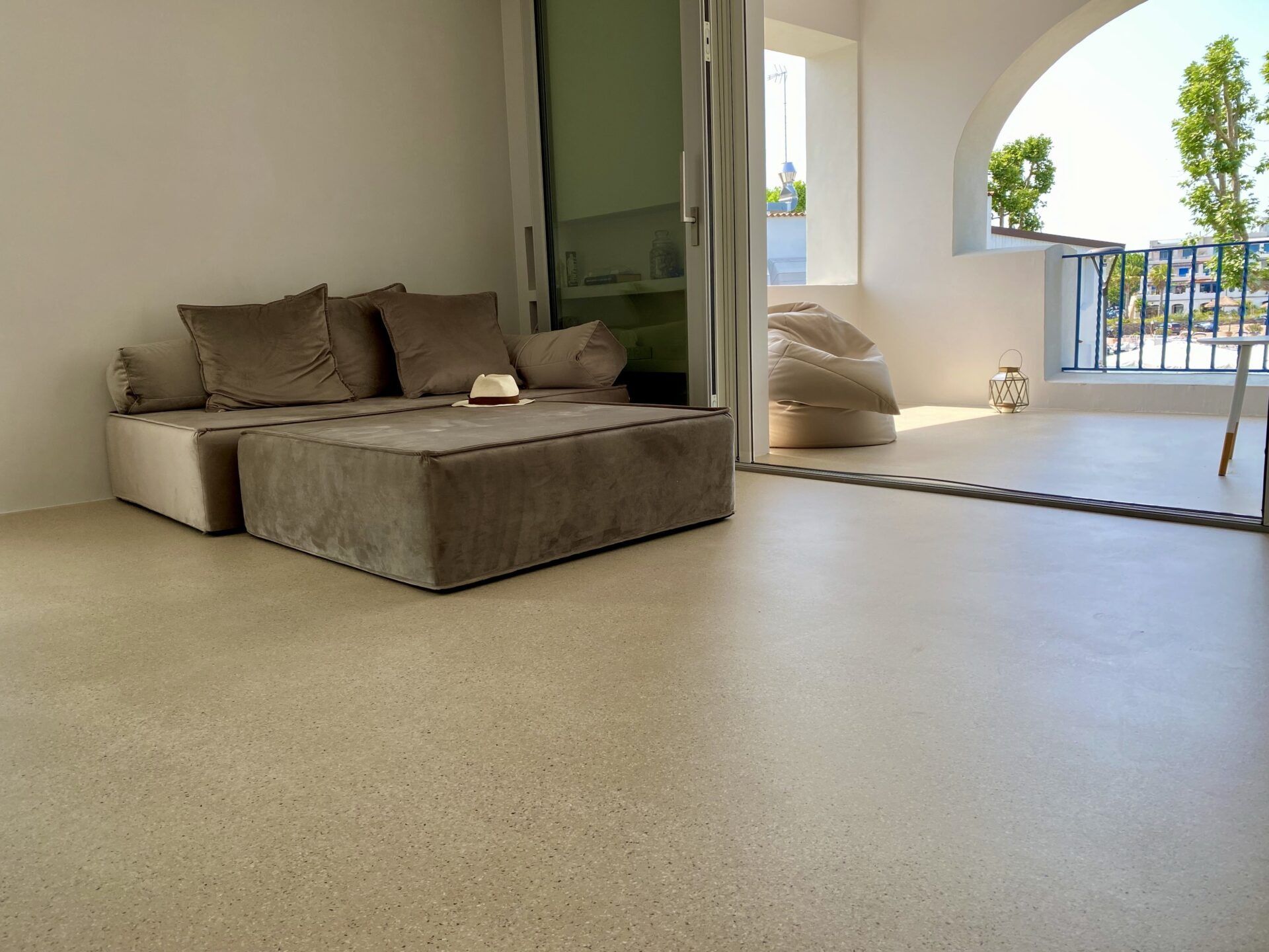 Soggiorno moderno con divano componibile beige, ampie finestre e vista dal balcone.