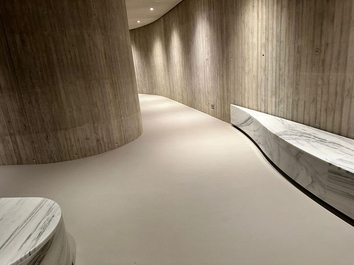 Corridoio curvo rivestito in legno con panche bianche e luci soffuse a soffitto.