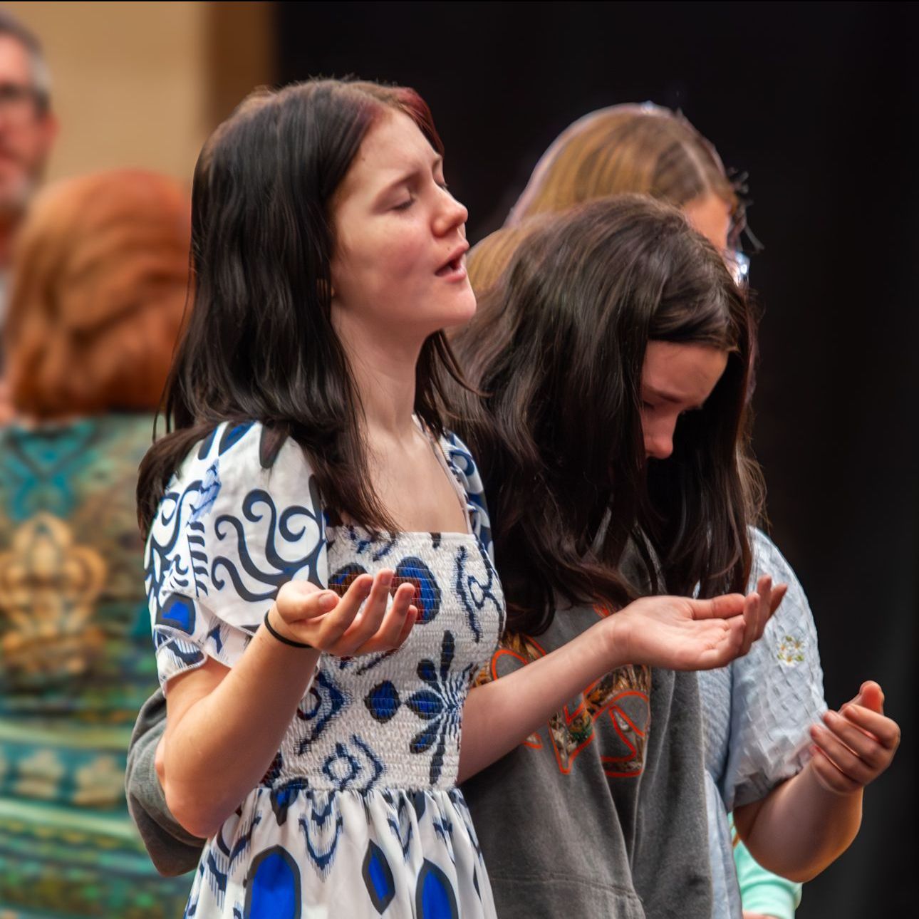 A woman in a blue and white dress holds her hands out in prayer