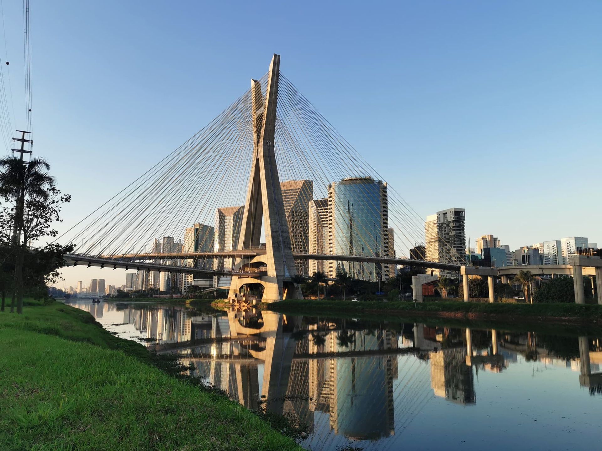 A Ponte Estaiada Octávio Frias de Oliveira reflete no Rio Pinheiros, com os arranha-céus da cidade ao fundo.