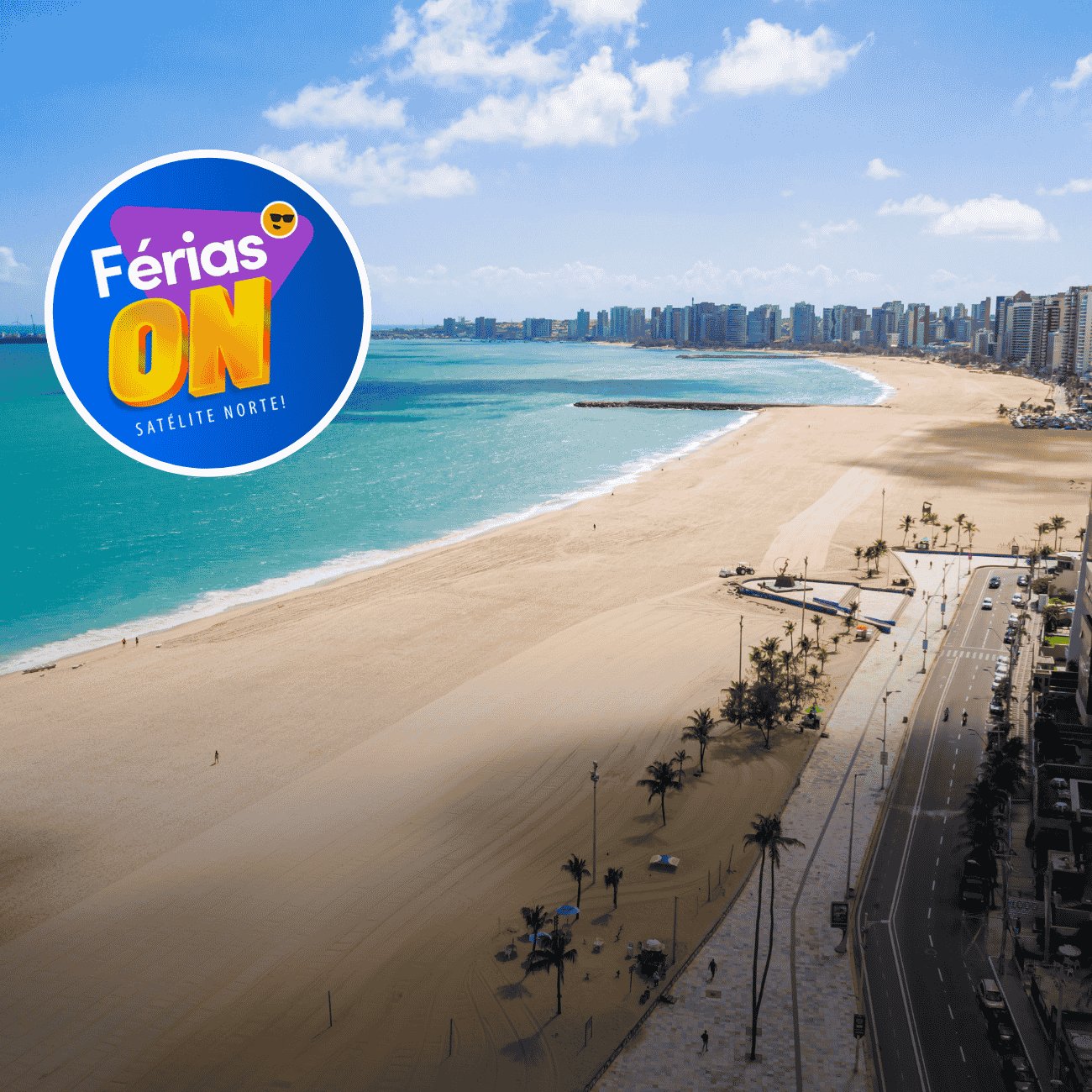 A imagem mostra uma vista aérea de uma extensa praia urbana em um dia ensolarado, com mar em tons de azul-turquesa e uma larga faixa de areia clara. Ao fundo, uma longa fileira de edifícios à beira-mar compõe o horizonte da cidade, enquanto a avenida litorânea, ladeada por coqueiros, acompanha toda a orla.