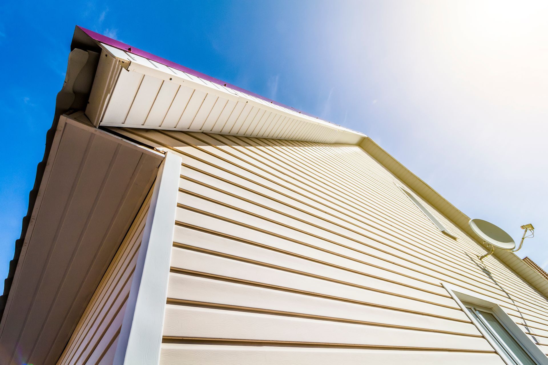 Beige vinyl siding on a house against a blue sky.