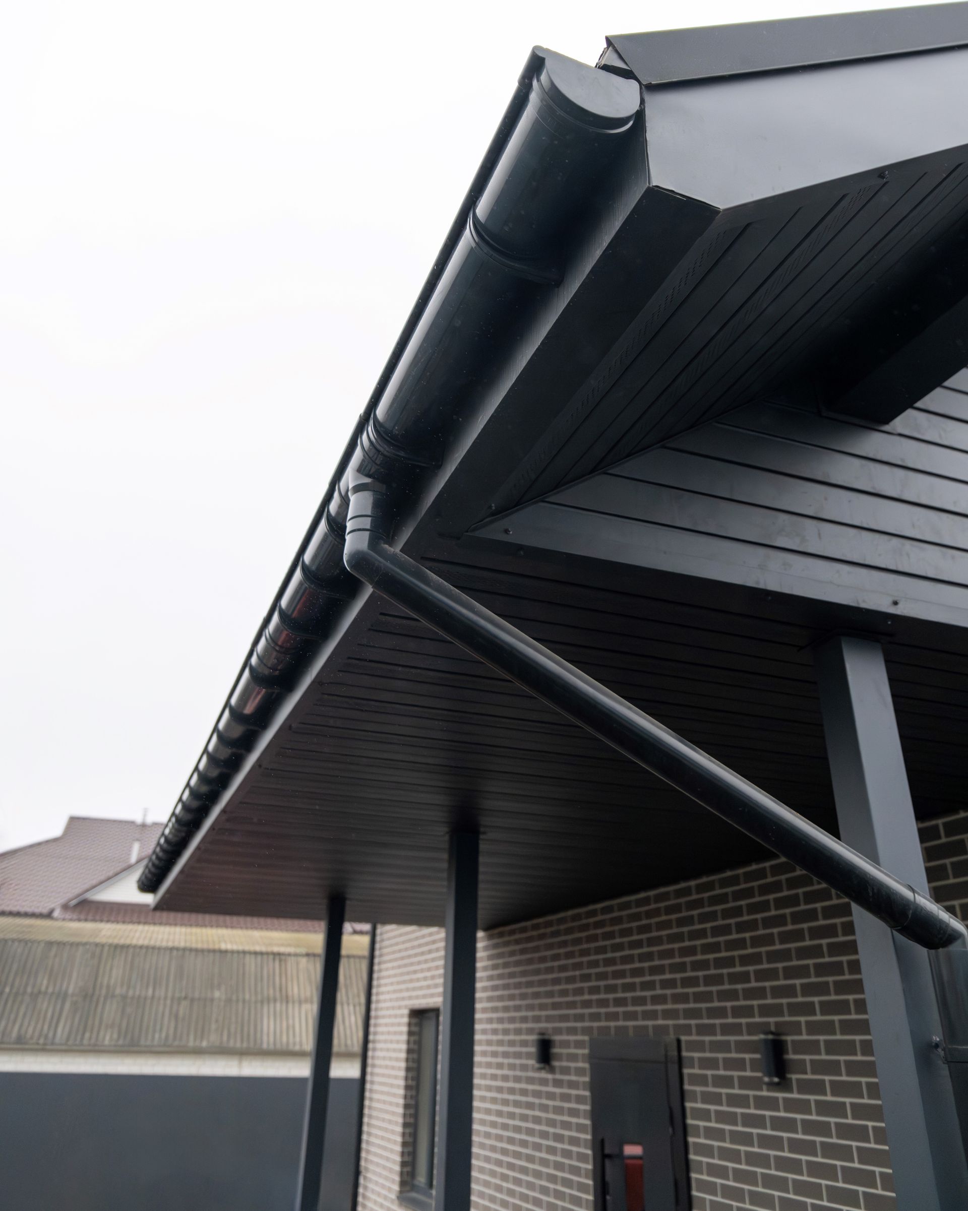 Black roof gutter system on a building with a dark-colored underside and brick exterior. Black roof gutter system on a building with a dark-colored underside and brick exterior.