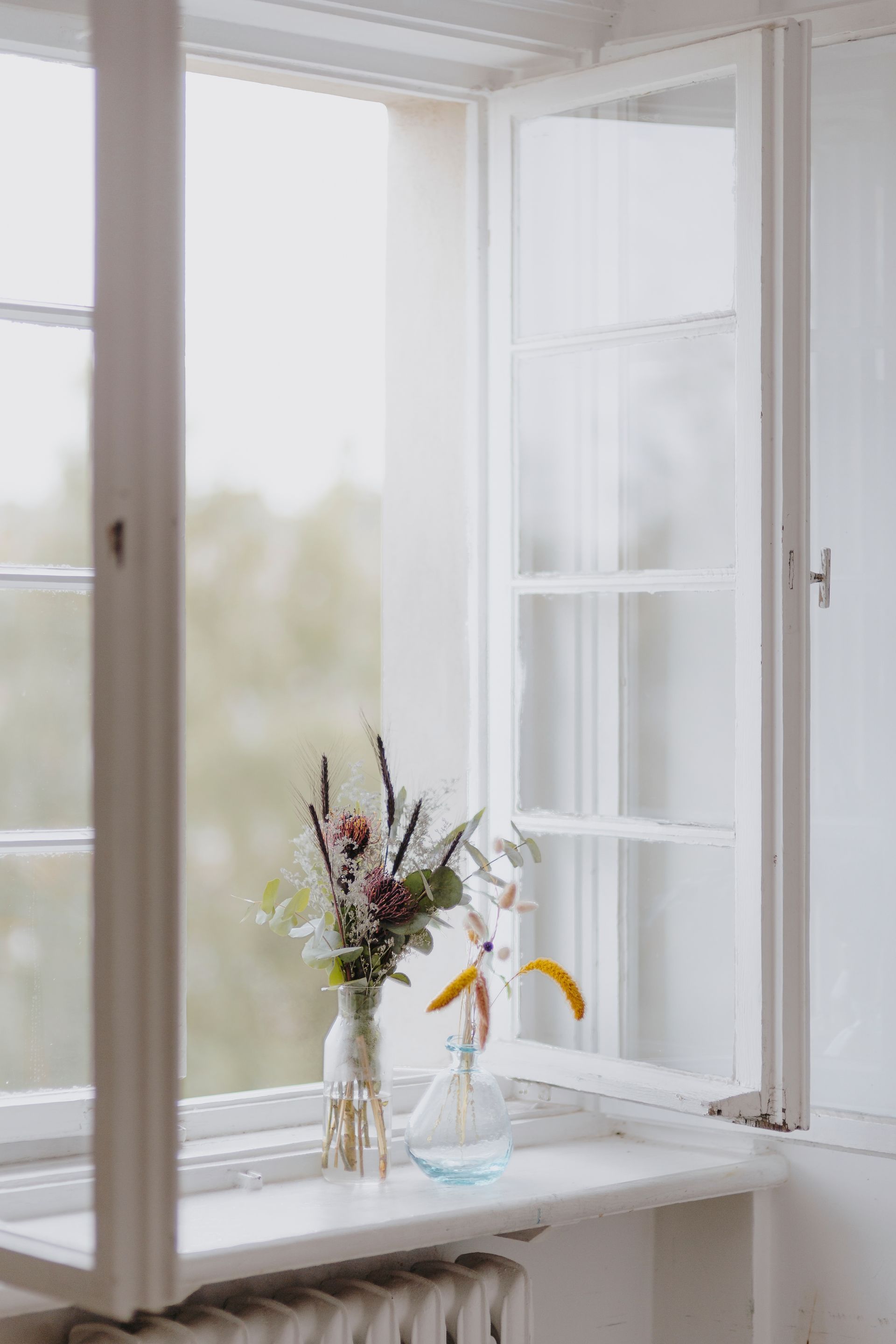Flowers in vases on a white windowsill, open window, blurry outdoor view. Flowers in vases on a white windowsill, open window, blurry outdoor view.