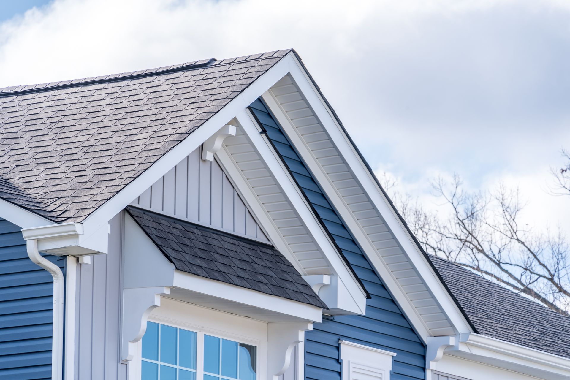 Blue house exterior with dark gray roof and white trim under a cloudy sky.