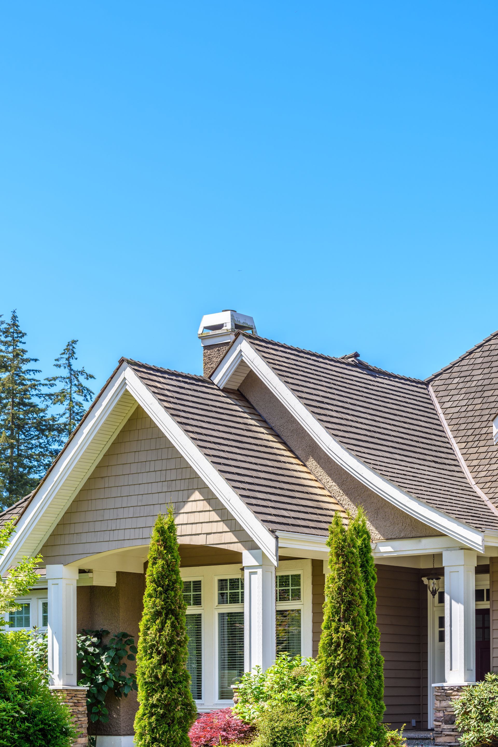 House exterior with brown roof, white trim, and two green trees in front, under a blue sky. House exterior with brown roof, white trim, and two green trees in front, under a blue sky.